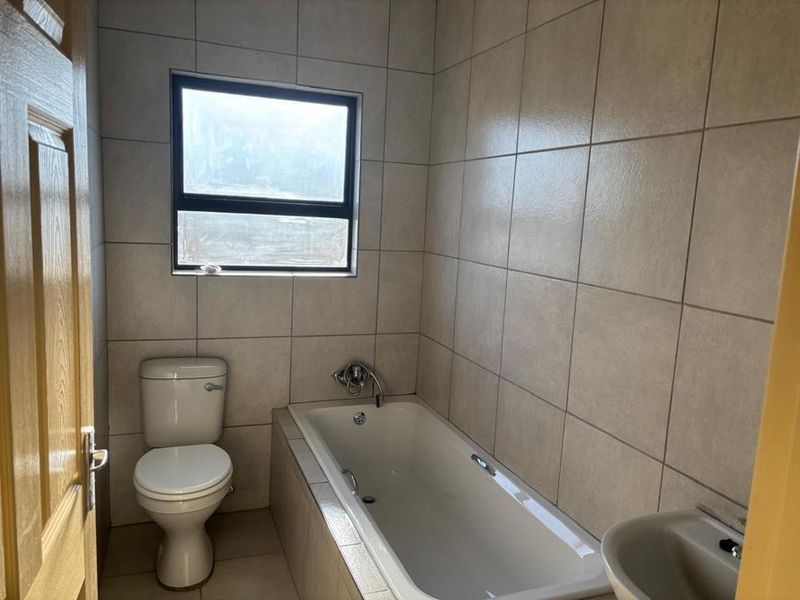 A functional bathroom featuring full-height wall tiling, a built-in bathtub, and a standard toilet, offering a clean and neutral space.