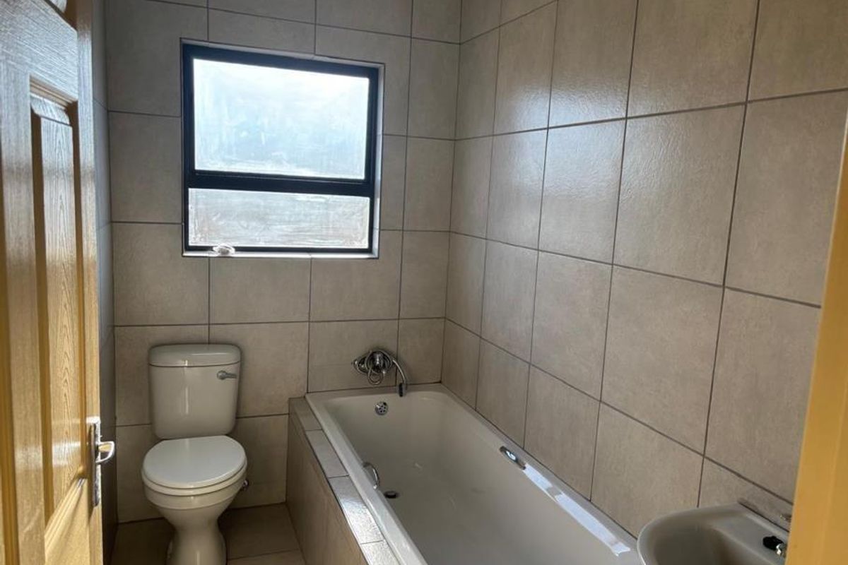 A functional bathroom featuring full-height wall tiling, a built-in bathtub, and a standard toilet, offering a clean and neutral space.