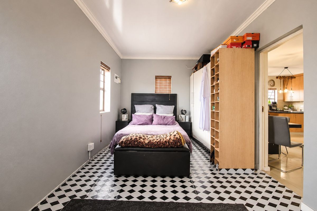 A bedroom featuring tiled flooring, coving, and built-in wardrobe storage, with an adjacent view into the kitchen area.