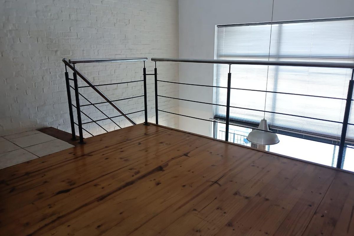 An open-plan mezzanine level featuring polished timber flooring, exposed white brickwork, and a modern metal balustrade overlooking the lower level.