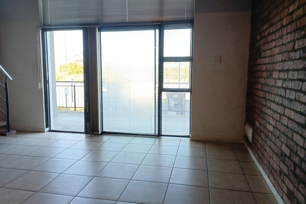 An empty living room featuring an exposed brick feature wall, tiled flooring, and large sliding glass doors leading to an outdoor balcony area.