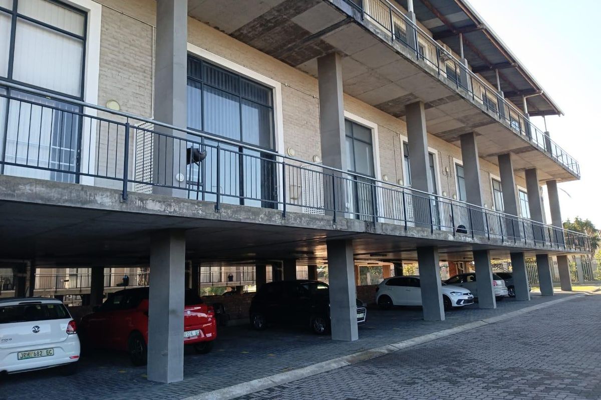 Exterior view of an apartment building featuring a covered ground-level parking area with concrete pillars and upper-level balconies with metal railings.