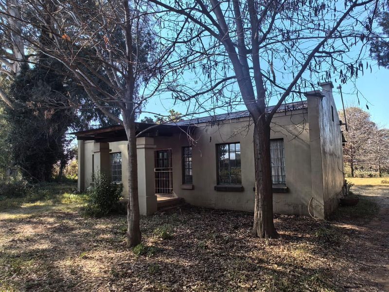 Front view of a single-story house featuring a covered porch, metal security gate, and multi-pane windows, set within a large, mature garden.