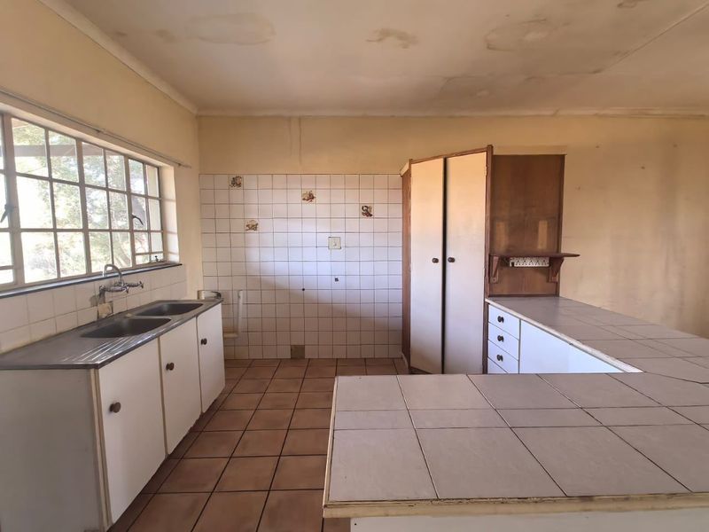 A dated, empty kitchen featuring tiled countertops, double basin sink, and built-in cabinetry, requiring cosmetic updates and ceiling repairs.