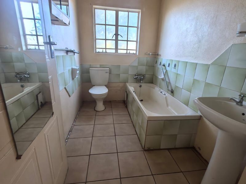 A dated bathroom featuring a pedestal basin, bathtub, and toilet with original ceramic tiling throughout.