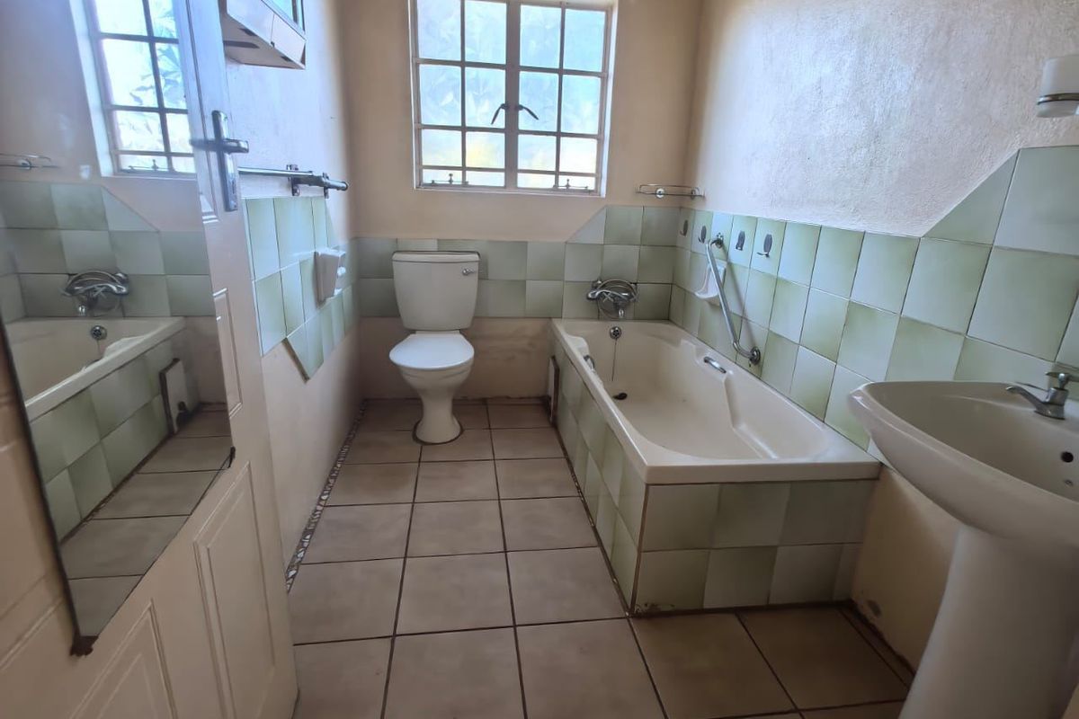 A dated bathroom featuring a pedestal basin, bathtub, and toilet with original ceramic tiling throughout.
