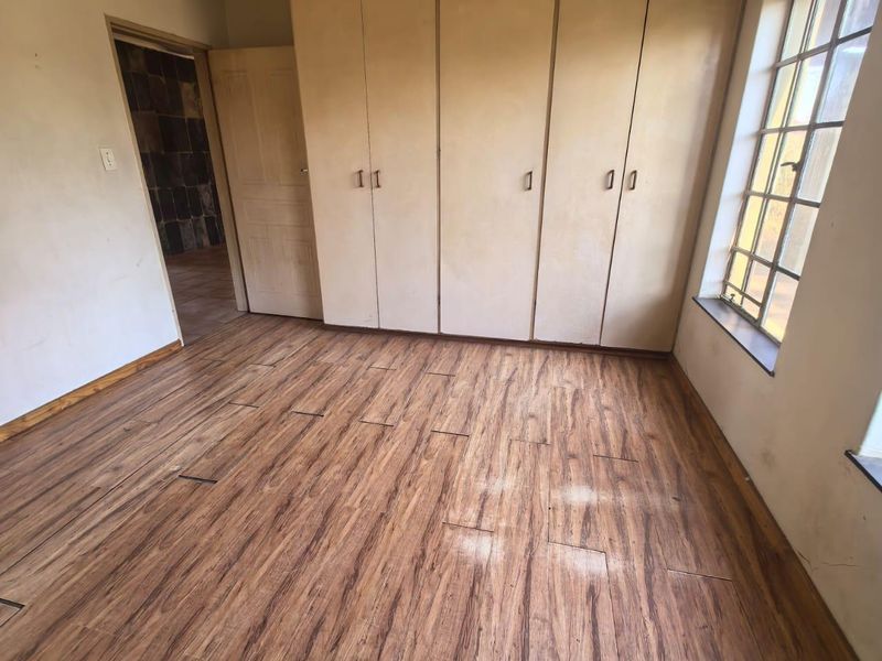 An empty bedroom featuring built-in cupboards, laminate flooring, and steel-framed windows, requiring cosmetic updates and ceiling repairs.