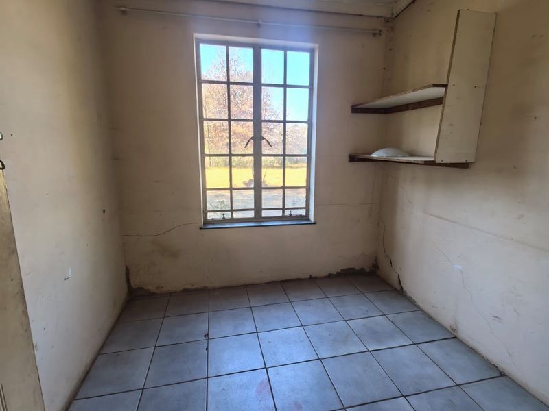An empty bedroom featuring tiled flooring, a grid-pattern window, and built-in wall shelving, requiring cosmetic updates and wall repairs.