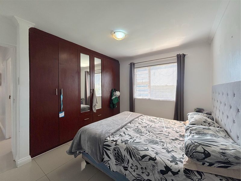 A well-lit bedroom featuring large dark wood built-in cupboards with mirrored panels, tiled flooring, and neutral wall finishes.