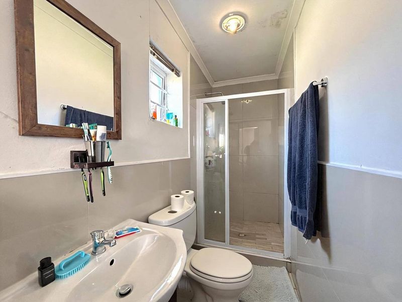 A functional bathroom featuring a shower enclosure, pedestal basin, and toilet, with neutral wall tiling and visible ceiling maintenance required.