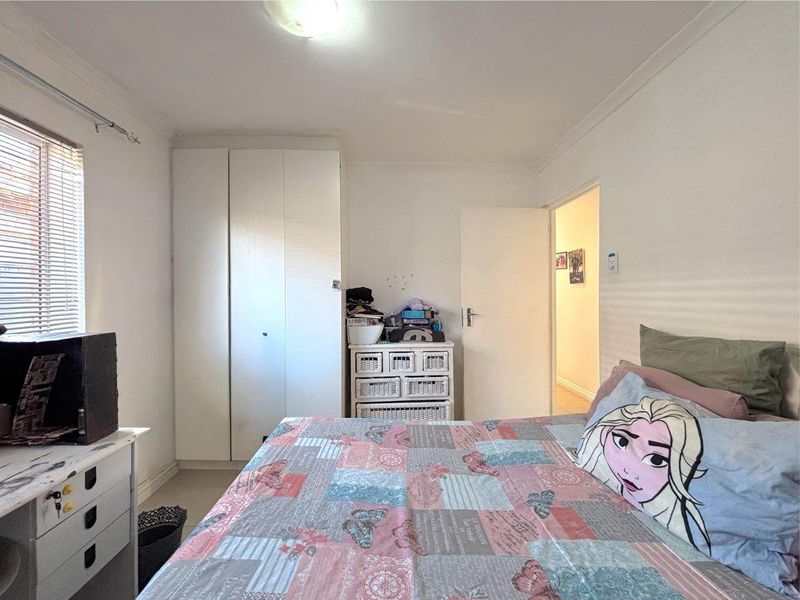 A functional bedroom featuring a built-in wardrobe, neutral wall finishes, and natural light through the window.