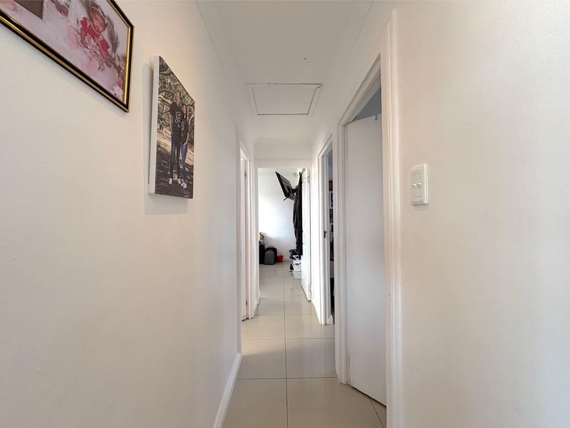 A clean, neutral hallway featuring tiled flooring and multiple doorways leading to various rooms within the home.