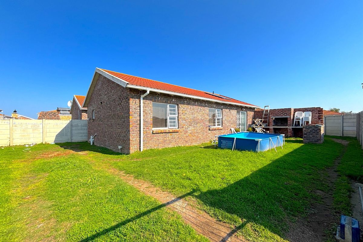 Rear view of a face-brick house featuring a tiled roof, built-in braai area, and a spacious garden with precast boundary walls.