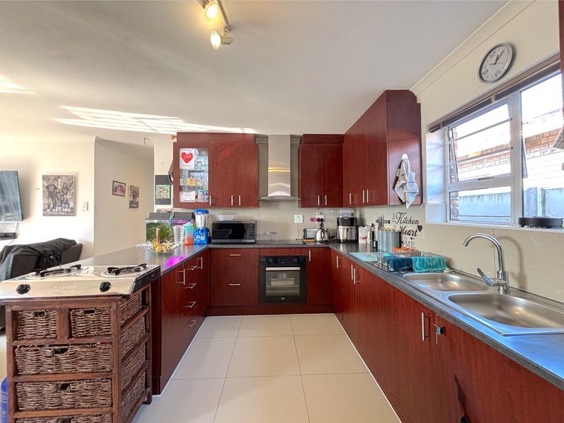 A functional U-shaped kitchen featuring dark wood cabinetry, stainless steel appliances, double sink, and tiled flooring, offering a practical layout for daily meal preparation.