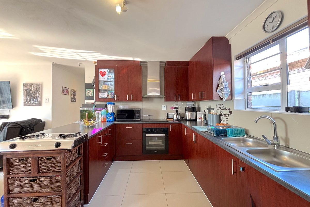 A functional U-shaped kitchen featuring dark wood cabinetry, stainless steel appliances, double sink, and tiled flooring, offering a practical layout for daily meal preparation.
