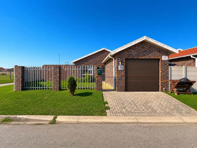 Front elevation of a face brick house featuring a single garage, paved driveway, and secure metal perimeter fencing.
