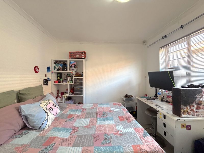 A functional bedroom featuring white walls, coving, and a window fitted with venetian blinds.