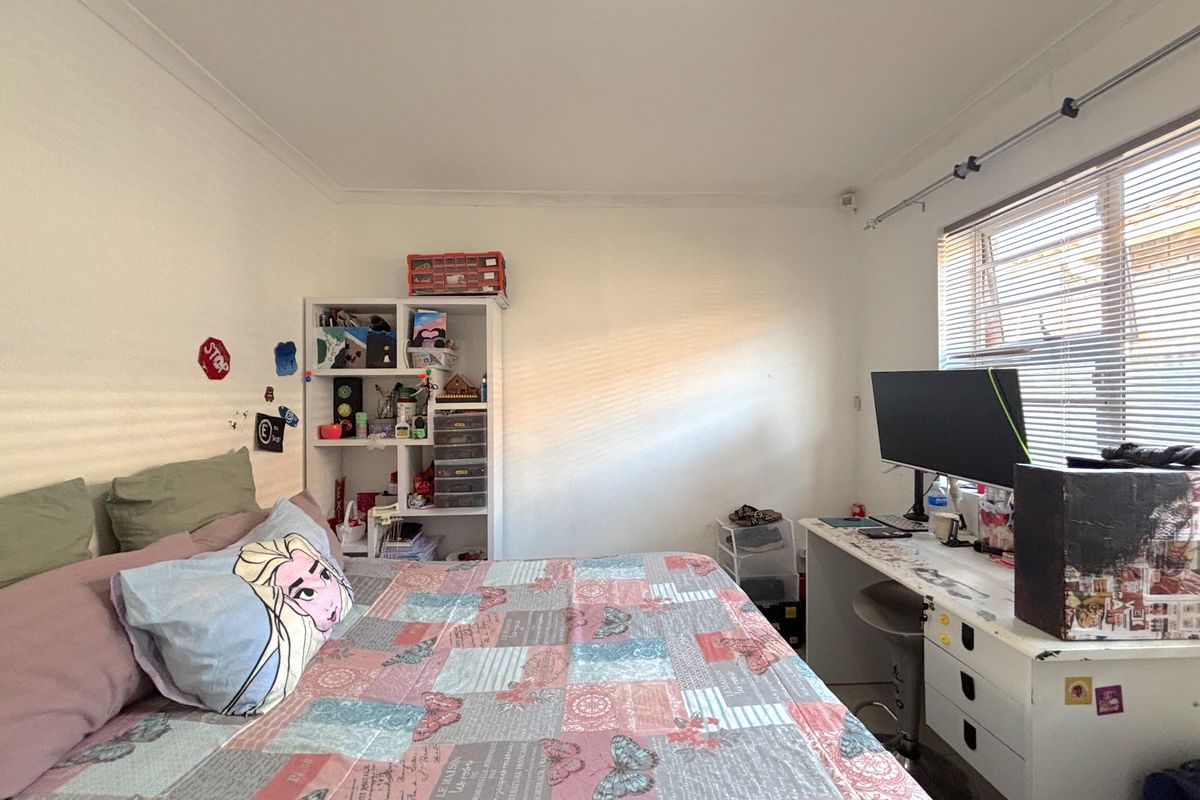 A functional bedroom featuring white walls, coving, and a window fitted with venetian blinds.