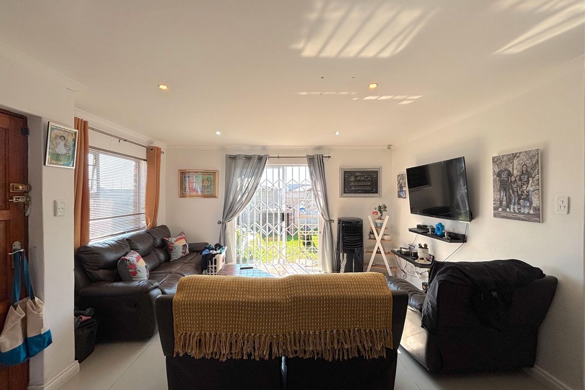 A bright living room featuring tiled flooring, recessed downlighting, and a sliding glass door with a security gate leading to the exterior.