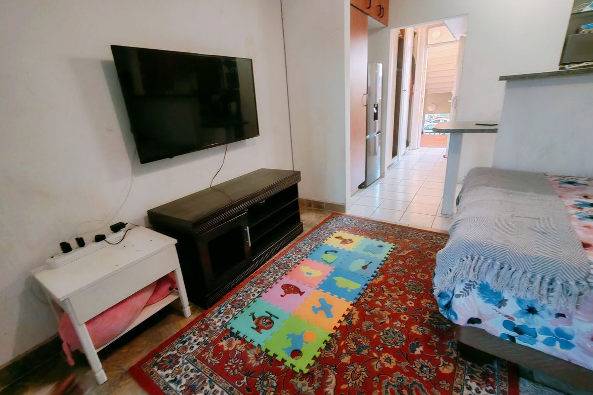 A living area featuring tiled flooring and built-in cabinetry, with a view leading into a hallway and adjacent kitchen space.