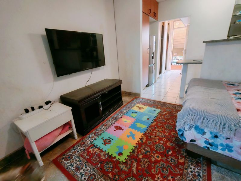 A living area featuring tiled flooring and built-in cabinetry, with a view leading into a hallway and adjacent kitchen space.