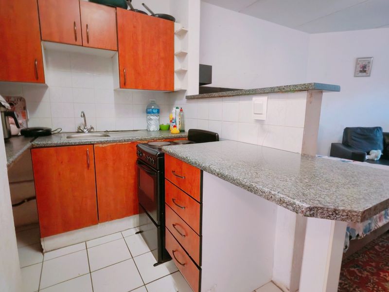 Compact kitchen featuring laminate cabinetry, granite countertops, a breakfast bar, and tiled flooring, offering a functional layout for an apartment setting.