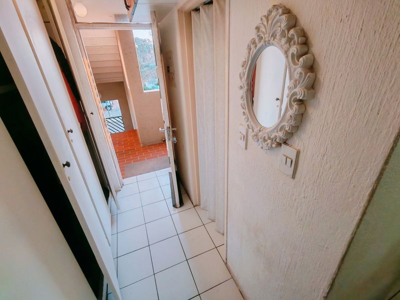A compact apartment hallway featuring tiled flooring and a built-in cupboard, leading directly to the building's exterior stairwell entrance.
