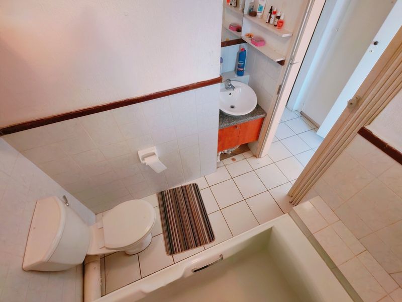 A functional bathroom featuring a bathtub, toilet, and vanity basin with built-in shelving, showing signs of wear and requiring cosmetic updates.