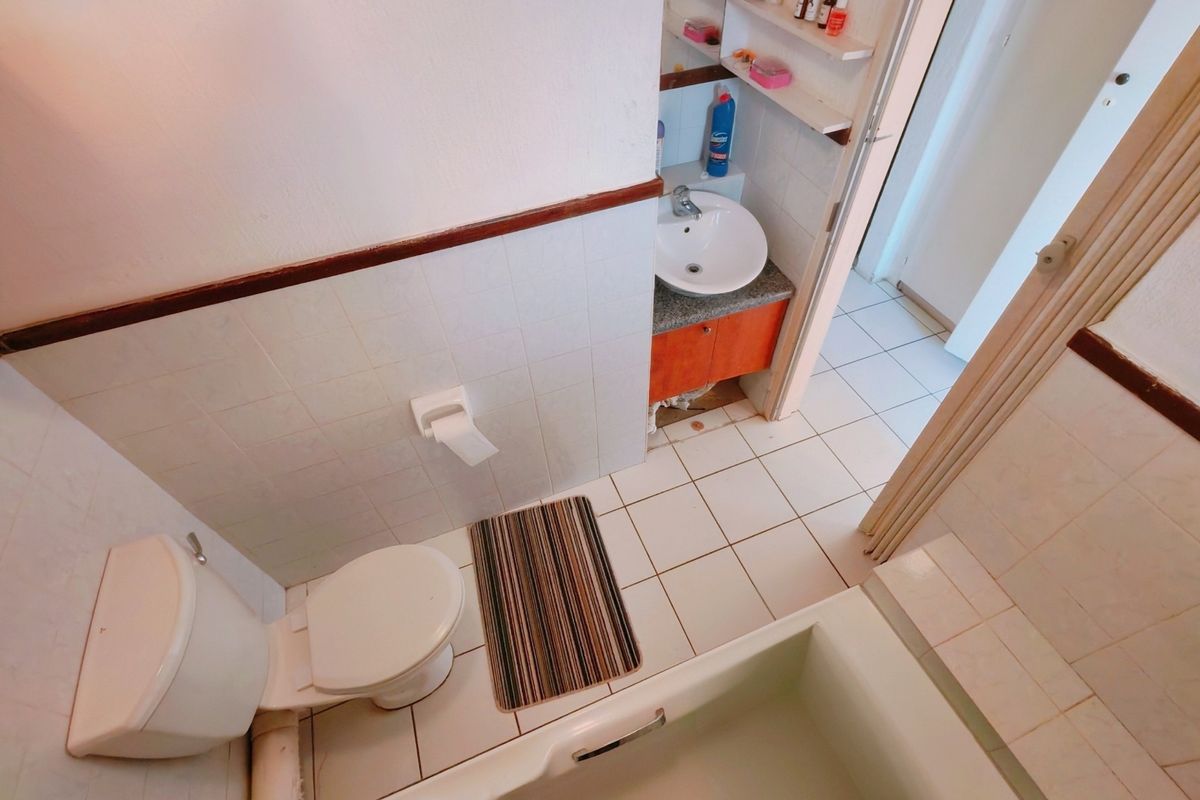 A functional bathroom featuring a bathtub, toilet, and vanity basin with built-in shelving, showing signs of wear and requiring cosmetic updates.