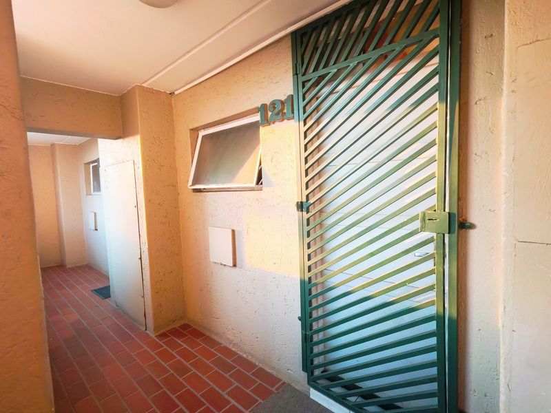 Apartment entrance area featuring a green security gate, tiled flooring, and a top-hung window.