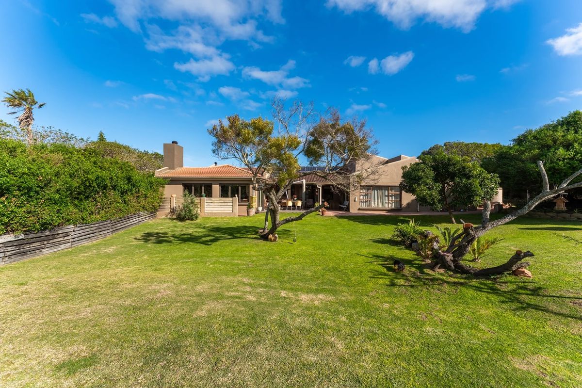 A spacious rear garden featuring a well-maintained lawn, mature trees, and a paved patio area attached to the main residence with solar panels.