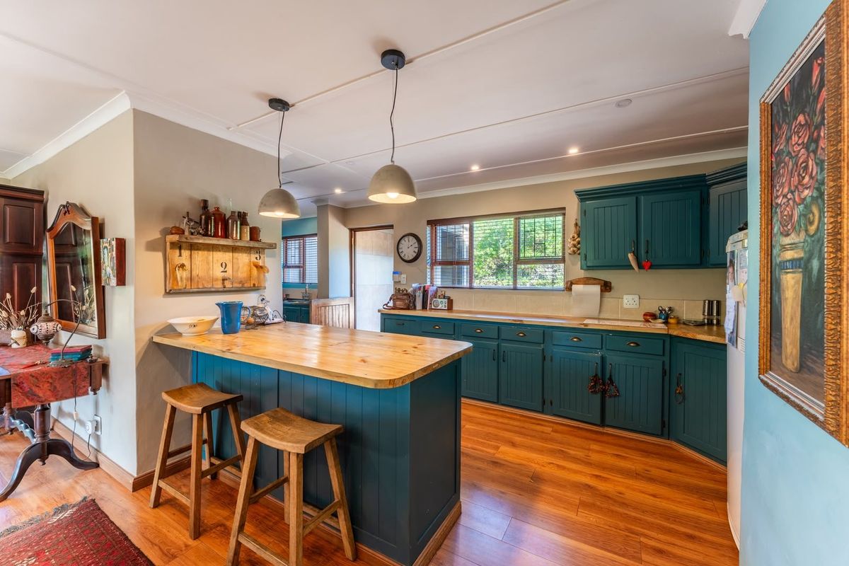 A functional kitchen featuring painted cabinetry, timber benchtops, a central island, and warm laminate flooring, offering a cozy and practical culinary space.