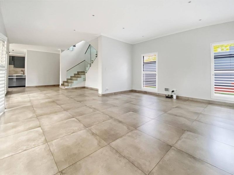 Spacious open-plan living area featuring large format floor tiles, a modern staircase with glass balustrade, and an integrated kitchen space.
