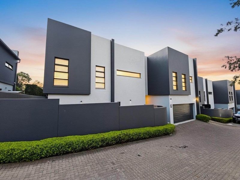 Modern multi-level residential facade featuring contemporary architectural design, paved driveway, integrated garage, and manicured boundary hedging.