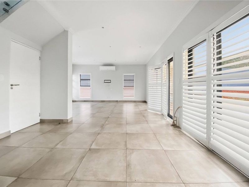 A bright, spacious, and empty living area featuring large format floor tiles, plantation shutters, and a wall-mounted split system air conditioner.