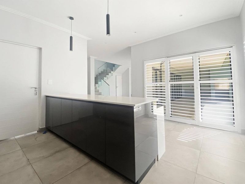 Modern kitchen area featuring a sleek dark island with stone countertop, tiled flooring, and large glass doors with integrated shutters.