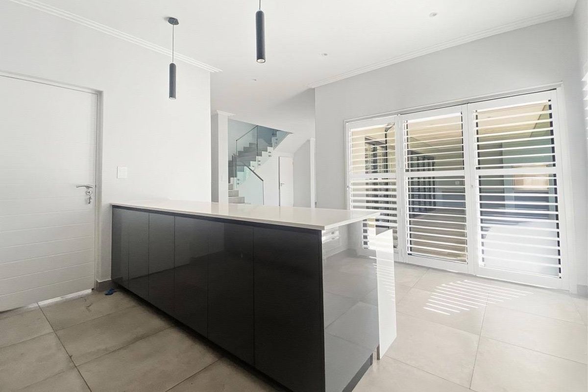 Modern kitchen area featuring a sleek dark island with stone countertop, tiled flooring, and large glass doors with integrated shutters.