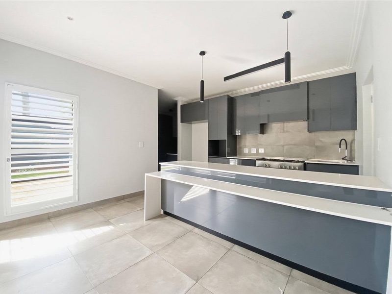 Modern kitchen featuring sleek grey gloss cabinetry, a stone breakfast bar, gas hob, and tiled splashback in a bright, open-plan layout.