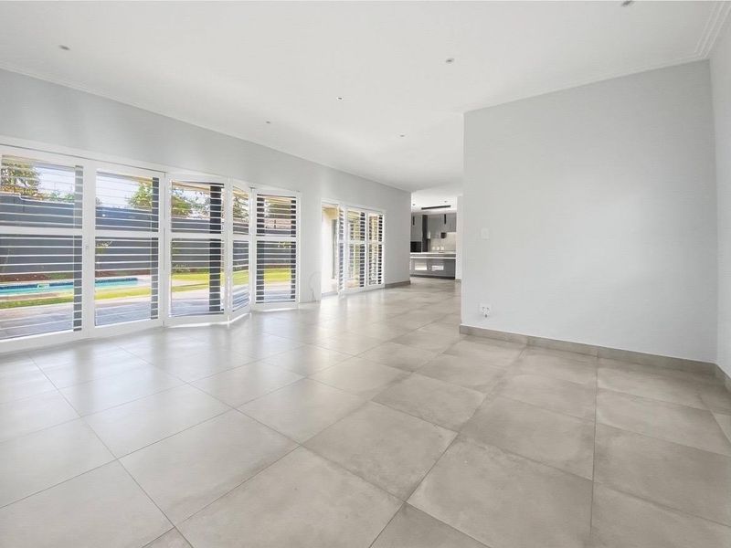 Spacious open-plan living area featuring large format floor tiles, recessed lighting, and expansive glass doors with plantation shutters leading to the outdoor area.