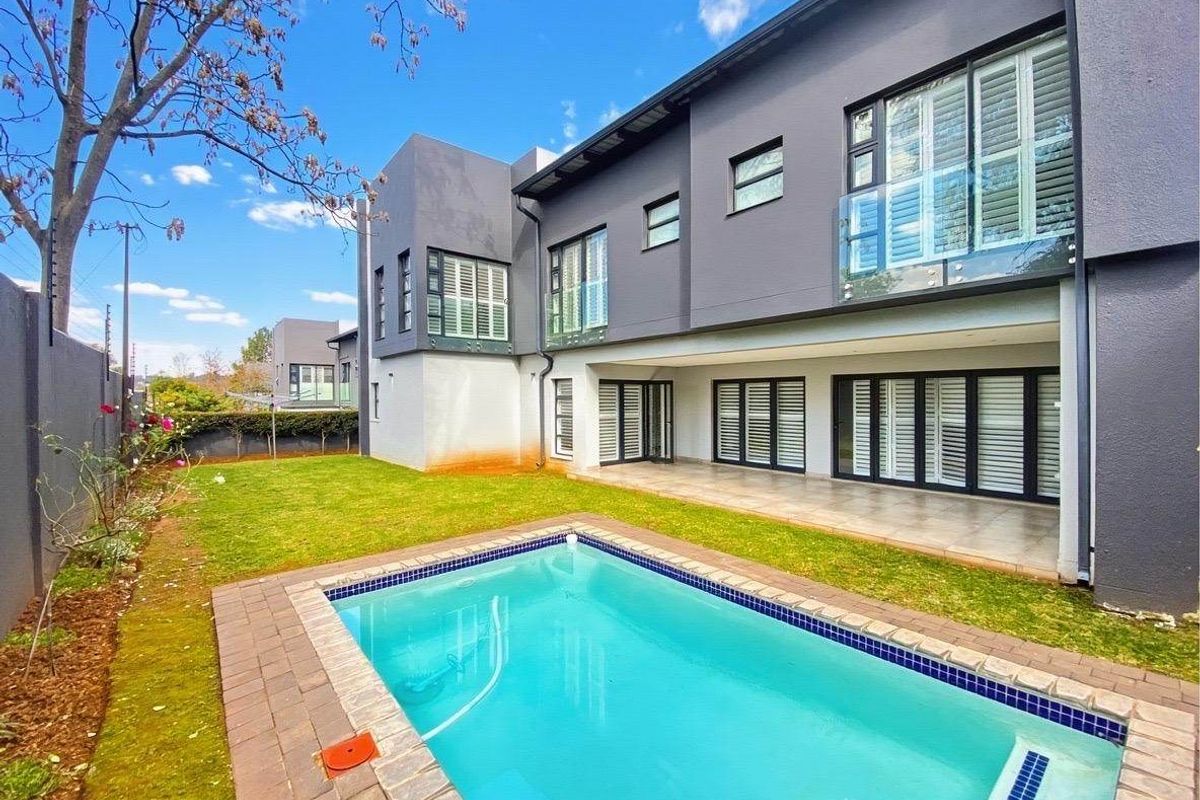 Rear exterior view featuring a swimming pool, paved surround, covered patio area, and modern two-story facade with glass balustrades.