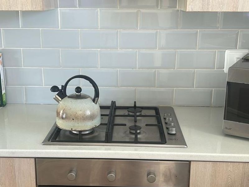A functional kitchen area featuring a built-in oven, gas hob, stainless steel extractor fan, and modern subway tile backsplash with light wood-finish cabinetry.