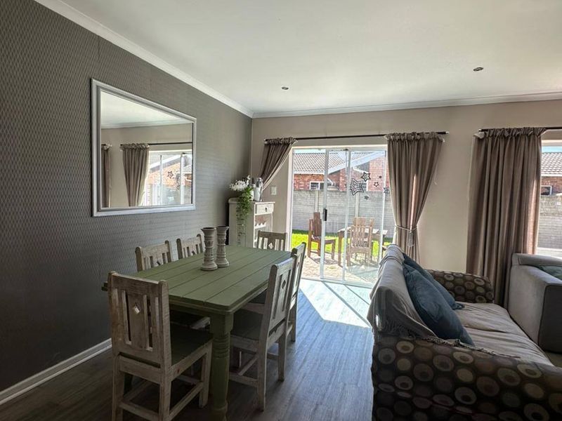 Open plan living and dining area featuring modern laminate flooring, textured feature wall, and sliding glass doors providing access to the rear patio.
