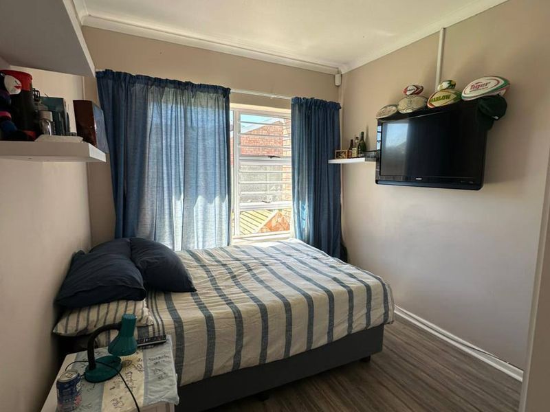 A compact bedroom featuring laminate flooring, wall-mounted shelving, and a louvered window providing natural light.