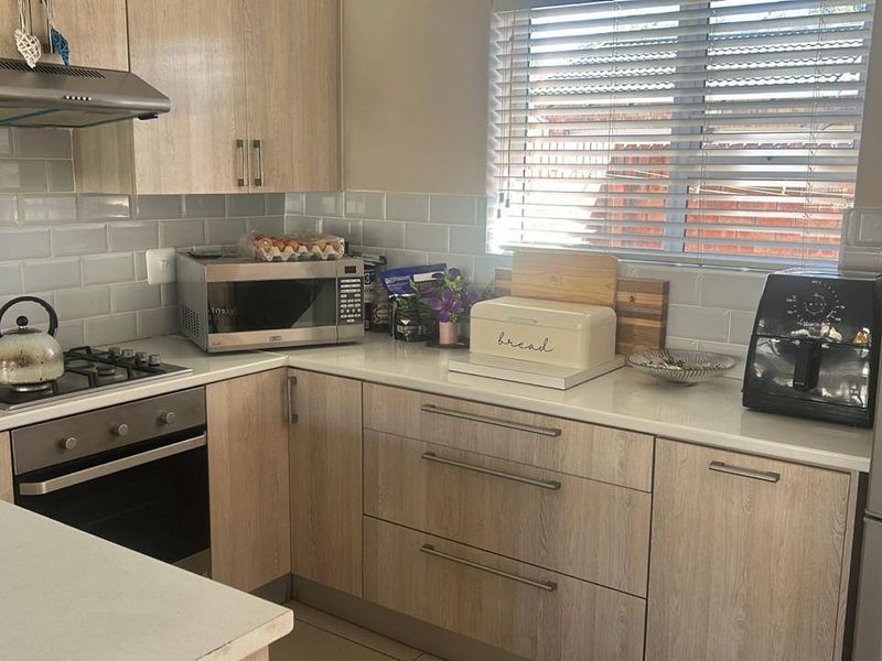 A functional kitchen featuring light wood-grain cabinetry, stone countertops, a subway tile backsplash, and integrated appliances including a gas hob and oven.