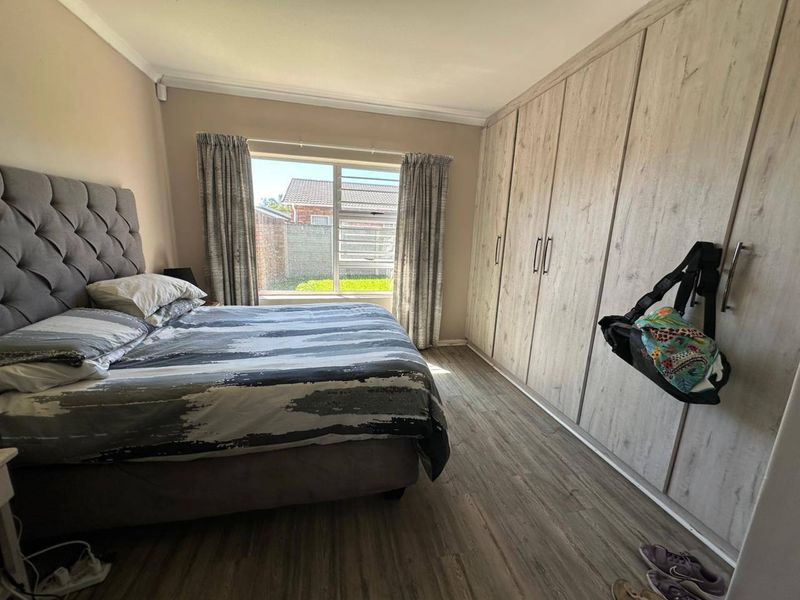 A well-maintained bedroom featuring light wood-look laminate flooring, extensive built-in cupboards, and a large window providing natural light.