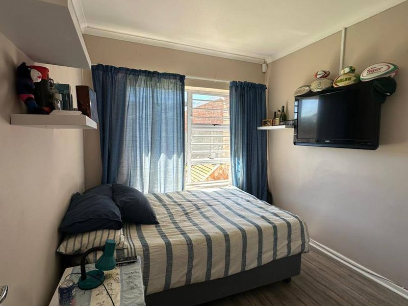 A compact bedroom featuring laminate flooring, neutral wall tones, and a window providing natural light.