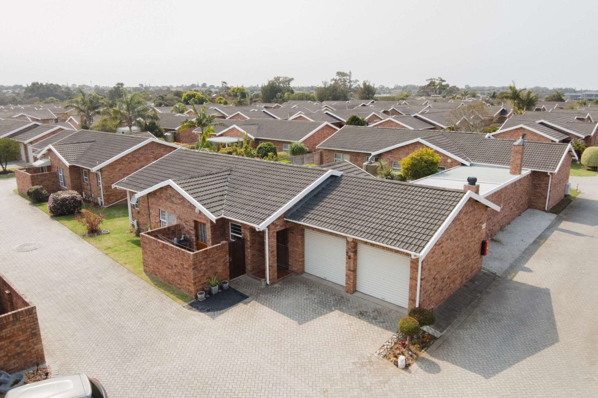 Aerial view of a brick townhouse complex featuring tiled roofs, double garages, and paved driveways within a residential estate.