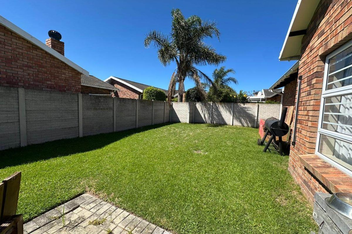 A private rear garden featuring a lawn, paved patio area, and enclosed by precast concrete boundary walls.