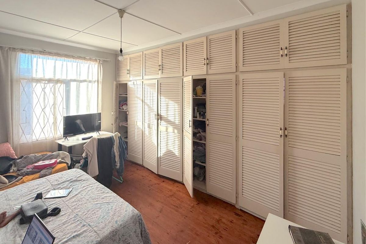 Bedroom featuring extensive built-in louvered cupboards and original timber flooring, offering ample storage space and a classic aesthetic.