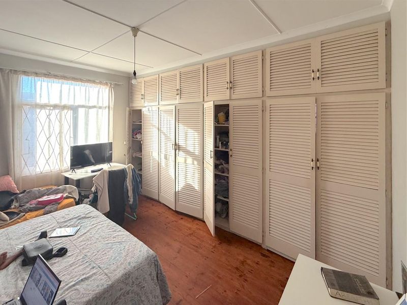 Bedroom featuring extensive built-in louvered cupboards and original timber flooring, offering ample storage space and a classic aesthetic.